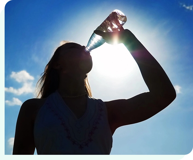 A woman drinking water from a bottle in the sun.