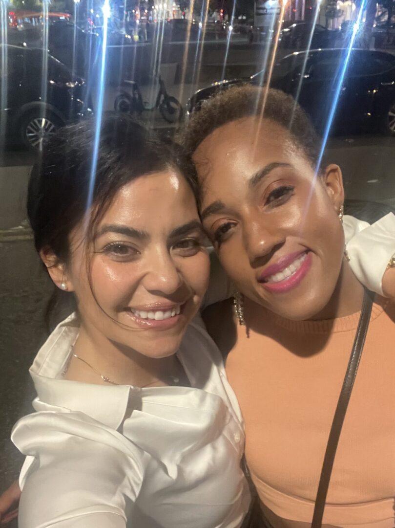 Two women smiling for a picture in front of some lights.