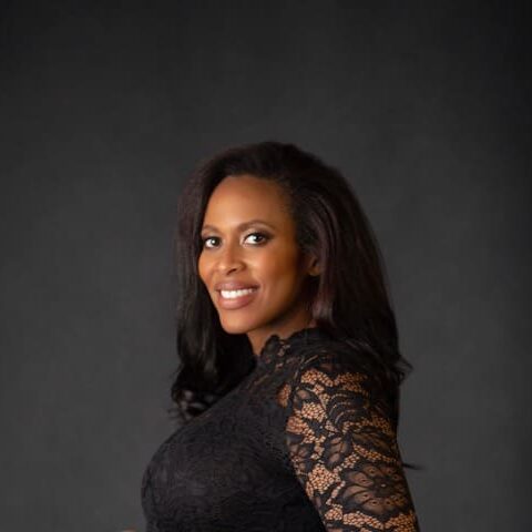 A woman in black dress standing next to wall.